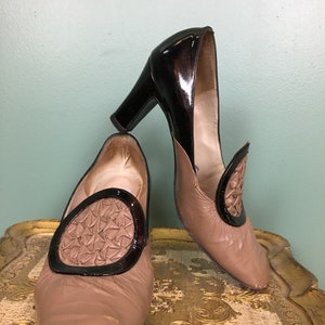K&ouml;nnte beinhalten: Ein Paar braune Lederschuhe mit schwarzen Lackleder-Akzenten. Die Schuhe haben eine quadratische Spitze und ein dekoratives Design auf der Vorderseite.