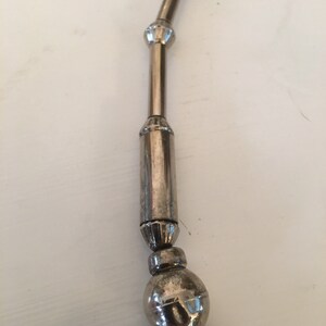 May include: A silver necklace with a series of round beads and cylindrical links. The necklace has a decorative design on the beads and links.