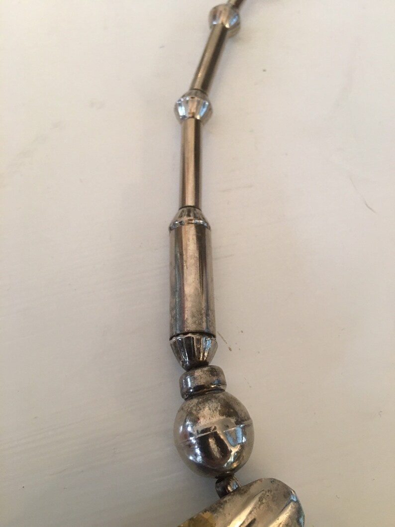 May include: A silver necklace with a series of round beads and cylindrical links. The necklace has a decorative design on the beads and links.