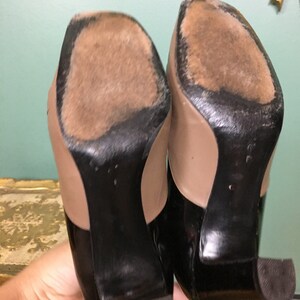 K&ouml;nnte beinhalten: Ein Paar schwarze und beige Pumps mit spitzer Zehenkappe. Die Schuhe haben ein schwarzes Lackleder-Obermaterial und einen beigefarbenen Lederabsatz.