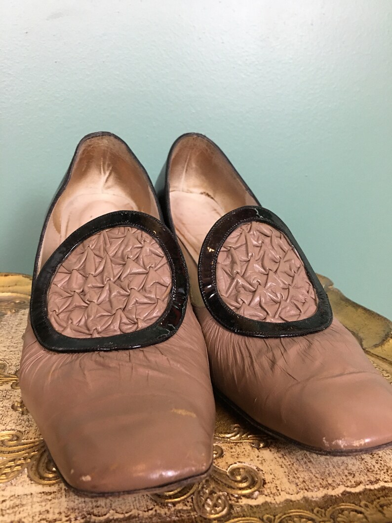 K&ouml;nnte beinhalten: Ein Paar braune Lederschuhe mit schwarzem Lacklederbesatz und einem dekorativen gewebten Design an der Spitze.