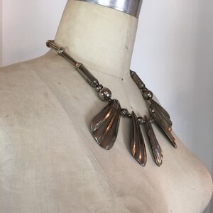 May include: A silver statement necklace with a geometric design featuring multiple fan-shaped pendants.