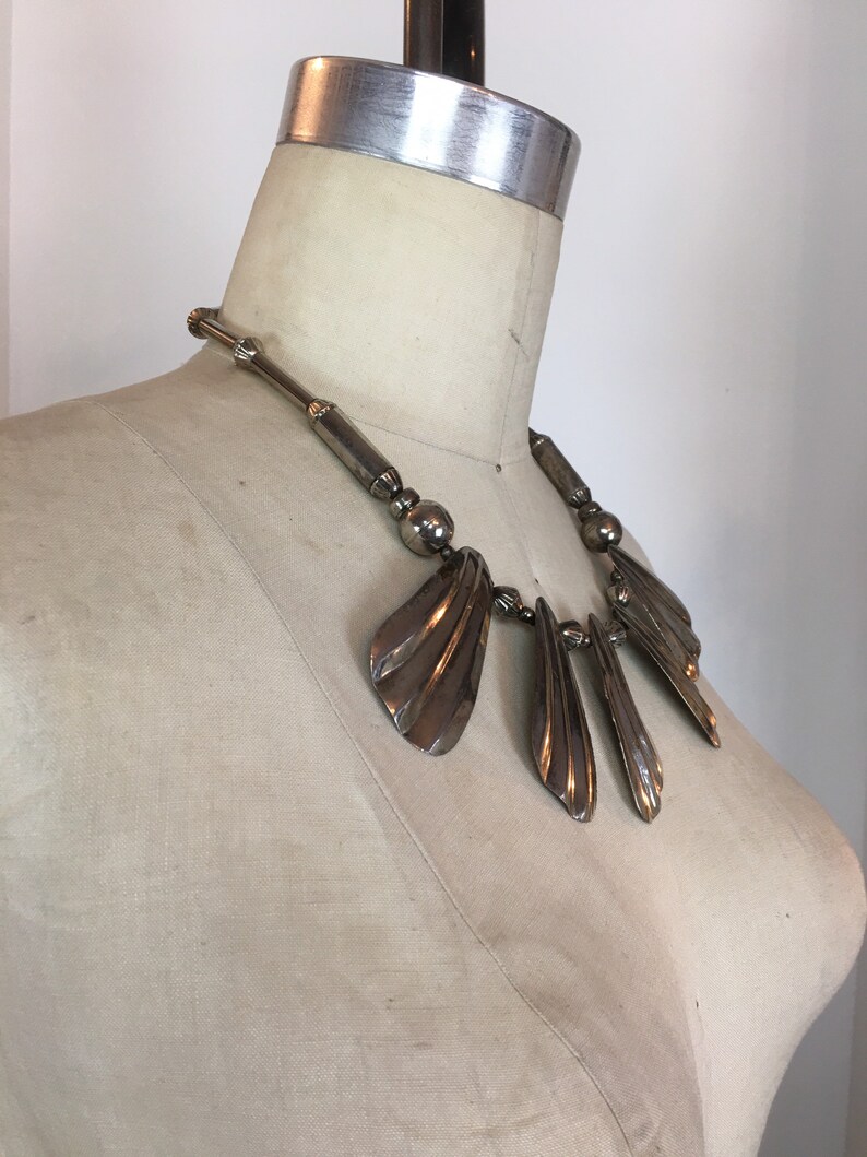 May include: A silver statement necklace with a geometric design featuring multiple fan-shaped pendants.