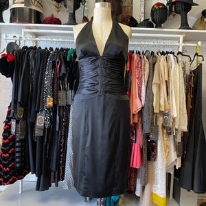 May include: A black halter dress with a fitted bodice and a straight skirt. The dress is made of a smooth, silky fabric.