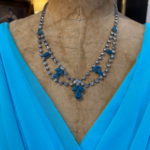 May include: A double strand necklace with blue and clear rhinestones. The necklace has a teardrop design with larger blue stones in the center.