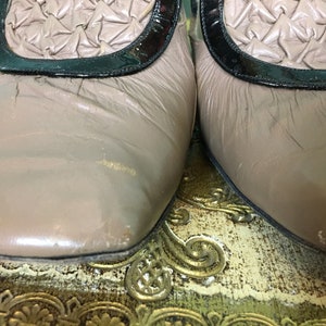 K&ouml;nnte beinhalten: Ein Paar hellbraune Lederschuhe mit schwarzem Lacklederbesatz und einem gewebten Design an der Spitze. Die Schuhe stehen auf einer gemusterten Oberfl&auml;che.