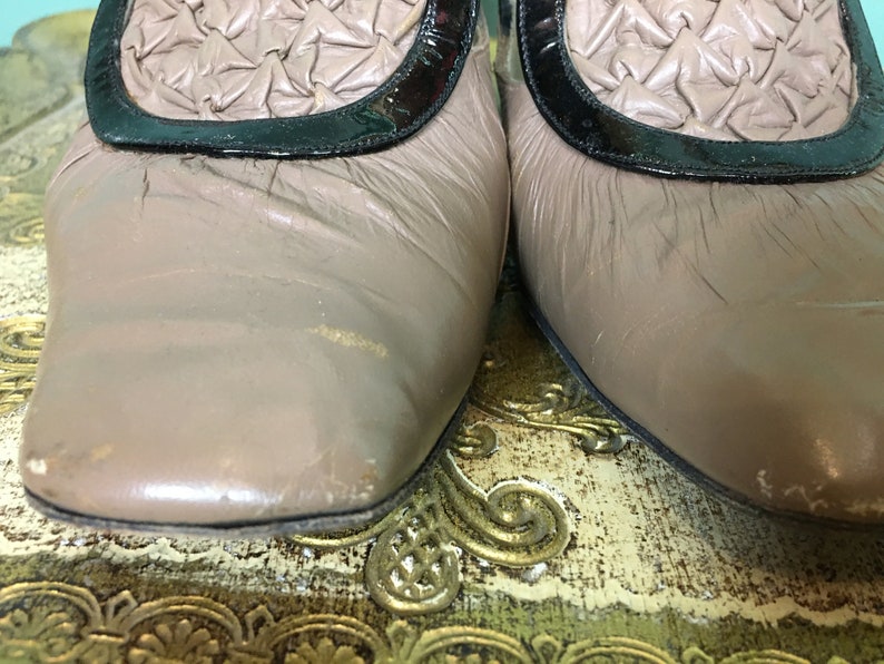 K&ouml;nnte beinhalten: Ein Paar hellbraune Lederschuhe mit schwarzem Lacklederbesatz und einem gewebten Design an der Spitze. Die Schuhe stehen auf einer gemusterten Oberfl&auml;che.