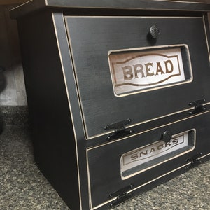 BREAD BOX The top compartment features a Frosted and Laser Engraved Plexiglass front saying "BREAD" and will fit 2 full size loaves. The other bin has a Plexiglass SNACKS and perfect for storing chips, cookies and so much more!