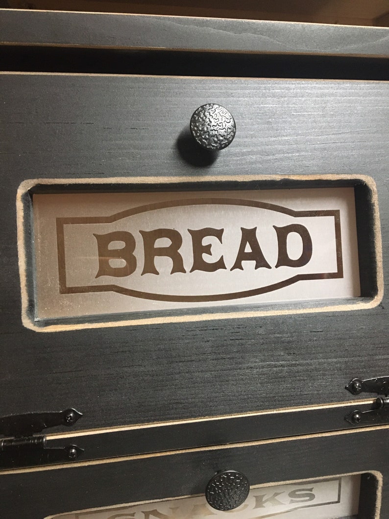 BREAD BOX The top compartment features a Frosted and Laser Engraved Plexiglass front saying "BREAD" and will fit 2 full size loaves. The other bin has a Plexiglass SNACKS and perfect for storing chips, cookies and so much more!