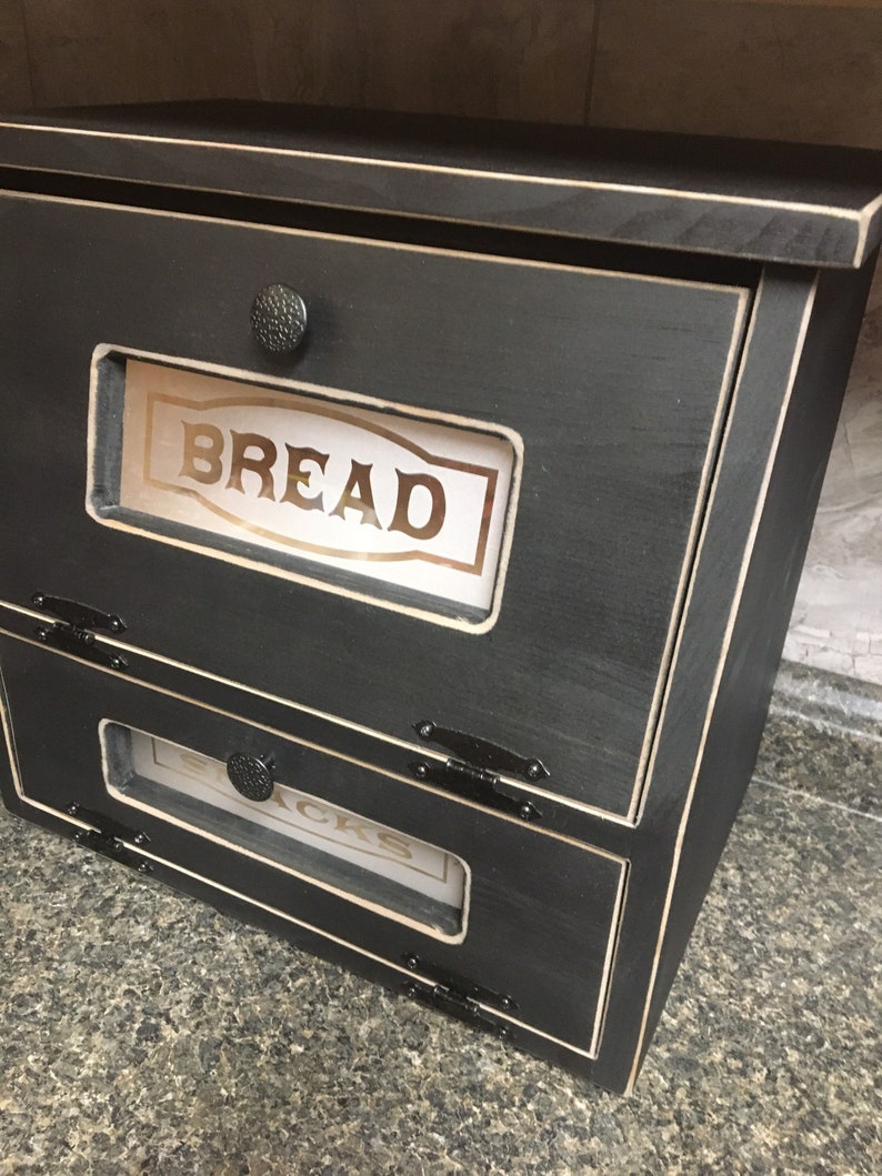 BREAD BOX The top compartment features a Frosted and Laser Engraved Plexiglass front saying "BREAD" and will fit 2 full size loaves. The other bin has a Plexiglass SNACKS and perfect for storing chips, cookies and so much more!