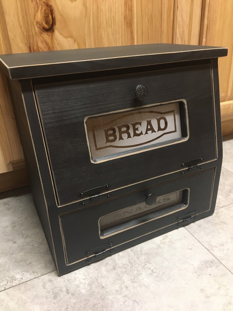 BREAD BOX The top compartment features a Frosted and Laser Engraved Plexiglass front saying "BREAD" and will fit 2 full size loaves. The other bin has a Plexiglass SNACKS and perfect for storing chips, cookies and so much more!