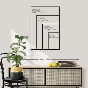 May include: A display of framed art prints in various sizes: 20x30in, 16x24in, 12x18in, and 8x12in. The image shows a black frame outline with the dimensions in inches and centimeters. The art is displayed above a wooden cabinet with a plant and fruit.