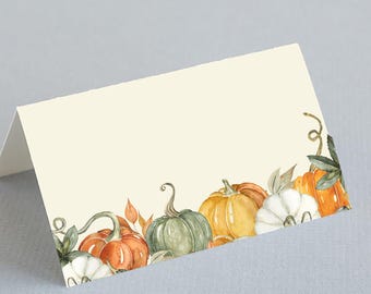 May include: Folded cream-colored place card with a watercolor design of pumpkins in shades of orange, green, yellow, and white. The pumpkins are arranged along the bottom edge, with green vines and leaves. Ideal for fall events.