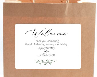 May include: A white welcome sign with black text and green foliage. The text reads "Welcome, Thank you for making the trip & sharing our very special day. Enjoy your stay! Love, Jaime & Scott"