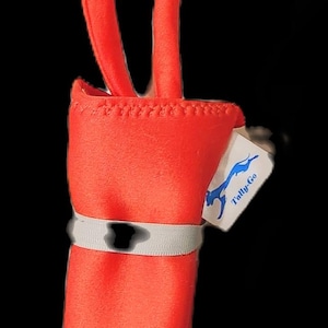 May include: A vibrant red wine bottle sleeve with two long, curved handles. A white band with a silver stripe encircles the sleeve. A small tag with the text "Tally-Go" is attached.