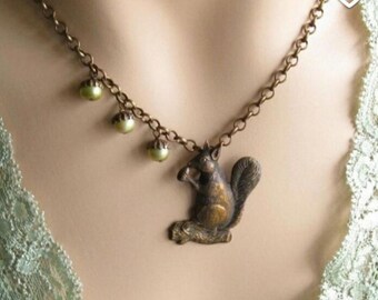 May include: A bronze necklace with a squirrel charm and green beads. The squirrel is holding a nut in its paws.