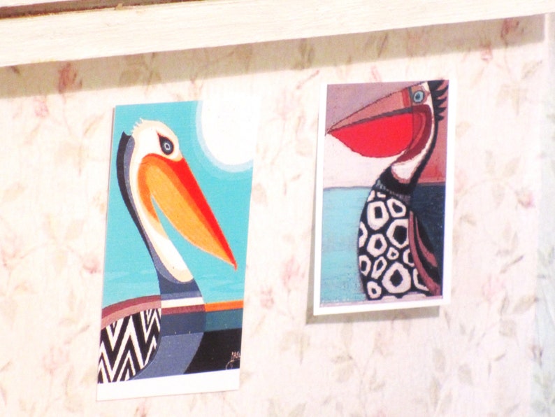 K&ouml;nnte beinhalten: Zwei bunte Vogel-Illustrationen auf wei&szlig;em Karton. Die linke Illustration ist ein Pelikan mit einem blauen, orangefarbenen und schwarzen Muster. Die rechte Illustration ist ein Vogel mit einem roten Schnabel und einem schwarz-wei&szlig;en Muster.