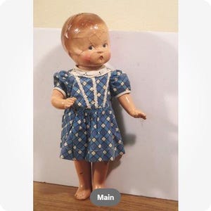 May include: A vintage doll with a cracked head and a blue and white patterned dress. The doll has a white collar and short sleeves. The doll's skin is a light peach color, and it has rosy cheeks.
