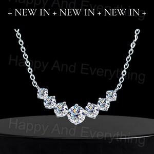 May include: A silver necklace with a curved row of five clear round cubic zirconia stones.
