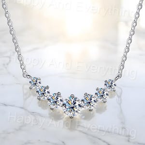 May include: A silver necklace with a curved row of six clear round cubic zirconia stones.