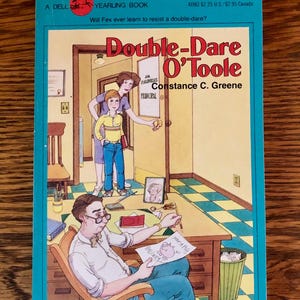 May include: A blue and yellow book cover with the title "Double-Dare O'Toole" by Constance C. Greene. The cover features an illustration of a boy and a woman in a school office.
