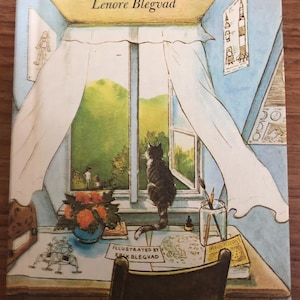 May include: Vintage book cover titled "Moon-Watch Summer" by Lenore Blegvad. The illustration depicts a cat looking out a window, with a desk, flowers, and drawings. The color palette includes blues, greens, and yellows, creating a nostalgic feel.