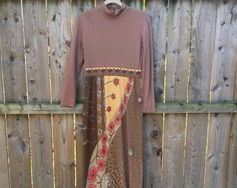 May include: A long brown dress with a high neck and long sleeves. The top half of the dress is a solid brown ribbed fabric. The bottom half of the dress is made of a patchwork of different brown and cream fabrics with a floral pattern.