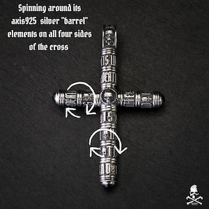 Pode incluir: Pingente de cruz prateada com elementos de caveira e barril. O texto "IS TO DEATH" é visível na cruz. A cruz está em um fundo escuro. O texto "Spinning around its axis925 silver "barrel" elements on all four sides of the cross" também é visível.