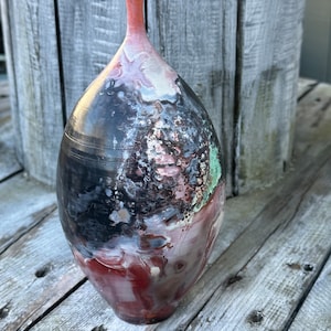 May include: A ceramic vase with a unique, abstract design. The vase is a dark brown color with splashes of red, white, and green.