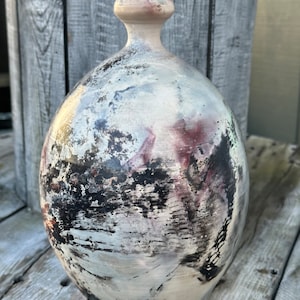 May include: A white ceramic vase with black and purple abstract patterns. The vase has a rounded body and a narrow neck.