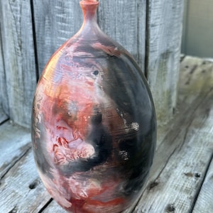May include: A ceramic vase with a rounded, oval shape. The vase has a black glaze with streaks of red, orange, and white.
