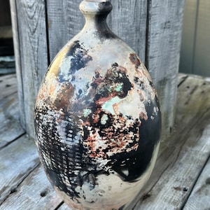 May include: A ceramic vase with a unique black, white, and brown abstract design. The vase has a rounded shape and a narrow neck.