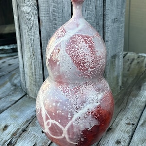 May include: A white and red ceramic vase with a unique, speckled glaze. The vase has a rounded, gourd-like shape with a narrow neck.