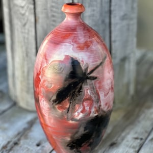May include: A red and white ceramic vase with a black butterfly design. The vase has a rounded shape and a narrow neck.