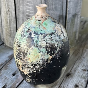 May include: A ceramic vase with a black, white, and green speckled glaze. The vase has a rounded body and a narrow neck.