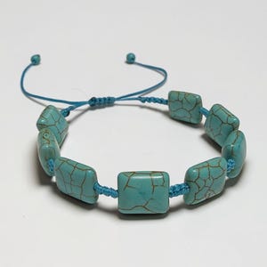 May include: A turquoise bracelet with rectangular beads and a blue adjustable cord. The beads have a cracked pattern and are strung together with a matching blue cord. The bracelet is displayed on a white surface.