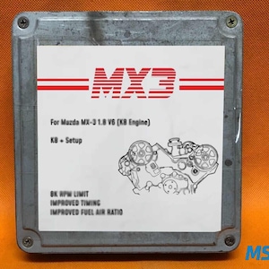Può includere: Un'unità di controllo elettronica (ECU) in metallo argentato con un'etichetta bianca con il testo "MX3" in rosso. L'etichetta include anche testo sul motore Mazda MX-3 1.8 V6, un diagramma del motore e miglioramenti delle prestazioni.