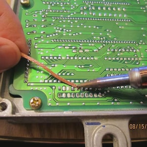 May include: A close-up of a green circuit board with copper wiring being soldered. A soldering iron is used to connect the wire to the board. The date 08/15/2011 is visible in the lower right corner.