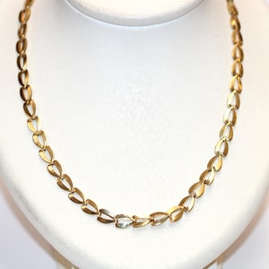 Könnte beinhalten: Eine goldfarbene Halskette mit einem sich wiederholenden herzförmigen Kettenglied-Design. Die Halskette wird auf einer weißen Büste präsentiert, die ihren zarten und eleganten Stil hervorhebt. Die Glieder sind eng miteinander verbunden und bilden ein durchgehendes Muster.