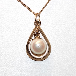 May include: A rose gold pendant necklace featuring a teardrop-shaped frame that encloses a single, round, iridescent white pearl. The pearl is suspended from a small jump ring within the centre of the smooth, polished metal teardrop pendant.