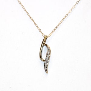 May include: A gold necklace featuring a slender, curved pendant. One side of the pendant is smooth polished gold, while the other side is set with a row of small, clear, sparkling stones. The pendant hangs from a delicate, thin gold chain.