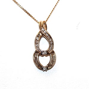 May include: A rose gold pendant necklace featuring a double-loop design. The upper loop is set with small round diamonds, while the lower loop contains baguette-cut diamonds. Two larger round diamonds are positioned at the center of each loop.