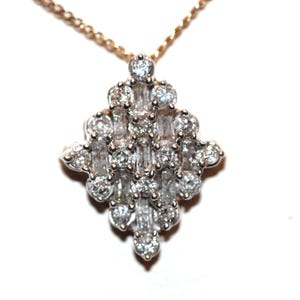 May include: A diamond pendant featuring a cluster of round and baguette-cut stones arranged in a geometric, diamond-shaped pattern. The pendant is set in a silver-toned metal and hangs from a delicate, thin gold-toned chain necklace.