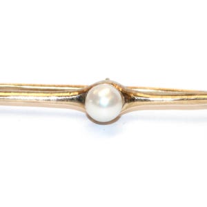 May include: A gold-coloured bar brooch featuring a central, round, white pearl. The brooch has a simple, elegant design, with a slightly curved bar and a secure clasp. This jewellery piece is suitable for various occasions.