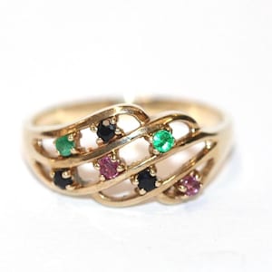 以下が含まれることがあります： 織り模様のデザインのゴールドトーンのリングで、複数の宝石がセットされています。リングには、緑、黒、ピンクの宝石が使用されています。白い背景にリングが表示されています。
