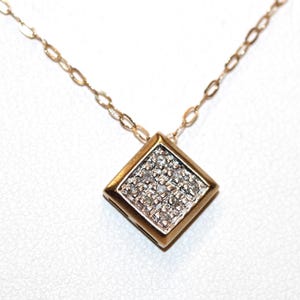 May include: A gold necklace featuring a square-shaped pendant. The pendant has a smooth gold border and a centre inlay set with nine small, clear, sparkling stones arranged in a grid pattern. The chain consists of delicate, oval-shaped gold links.