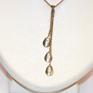 May include: A gold-coloured necklace featuring a fine chain and three teardrop-shaped pendants. The pendants have a cut-out design. The necklace is displayed on a white bust.