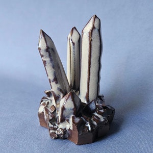 May include: A ceramic sculpture of three white and brown crystals clustered together on a brown base.