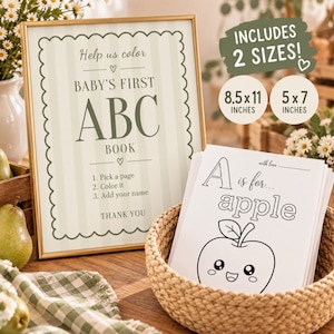May include: A framed sign with sage green stripes and scalloped edges reading Help us color BABY'S FIRST ABC BOOK, with instructions to pick a page, color it, and add your name. Next to it is a stack of coloring pages in a basket, including an A is for apple page.