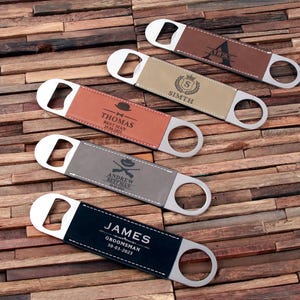 May include: Four personalised bottle openers with leatherette handles. The handles are brown, beige, grey, and black. The text on the handles reads "Alex", "Smith", "Thomas Best Man", "Andrew Best Man", and "James Groomsman".